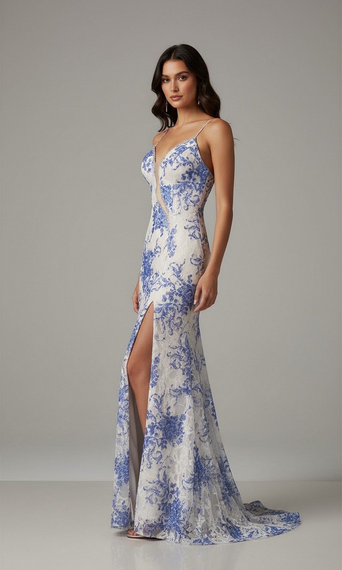 A woman models the Dave and Johnny 12950 long prom dress—a white gown with blue floral patterns, thin straps, a thigh-high slit, and a train—while standing against a plain gray background.